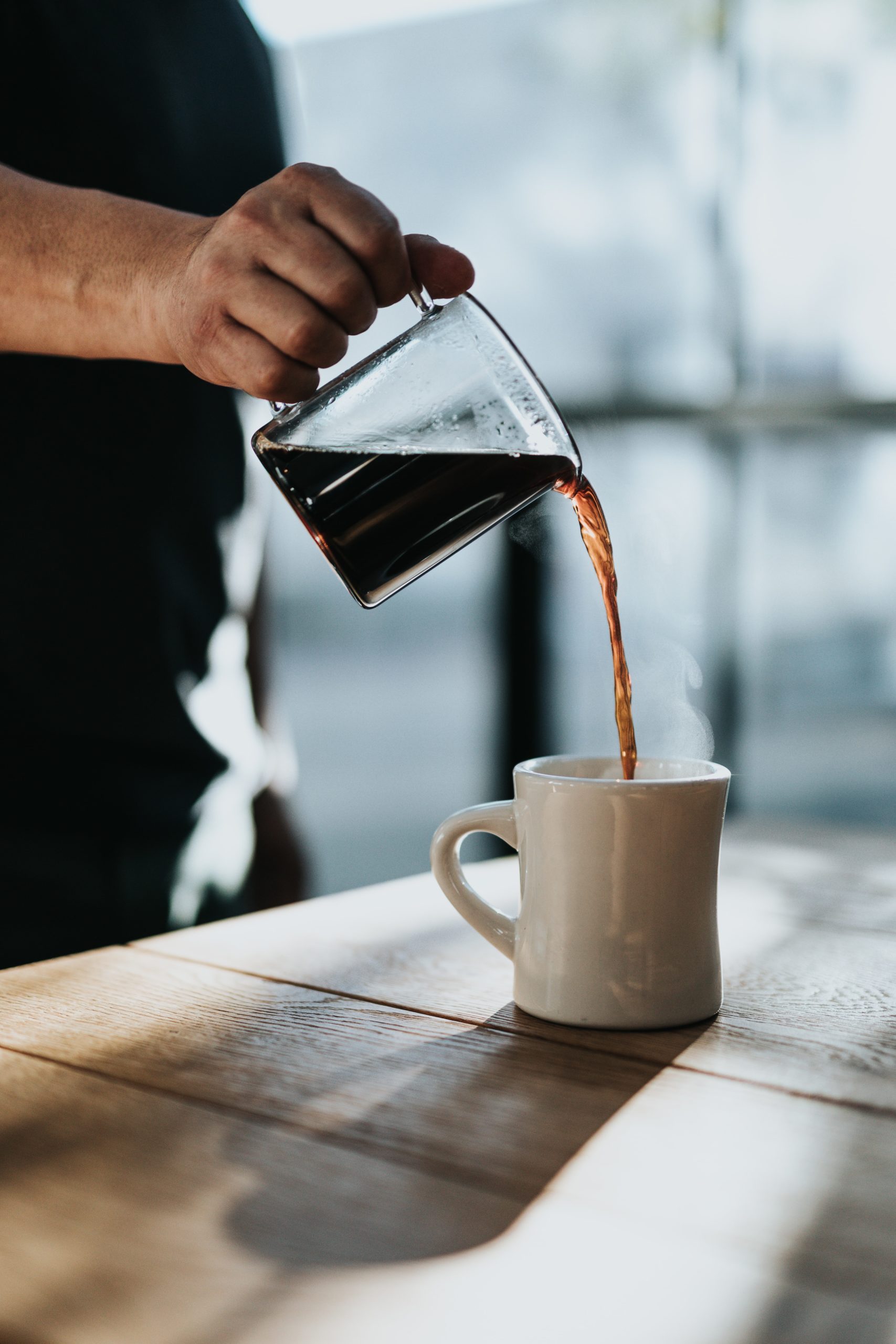 Kaffekanne med kaffe fyller opp kaffekopp