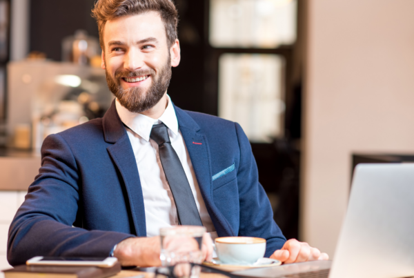 en mann sitter med laptop og drikker kaffe