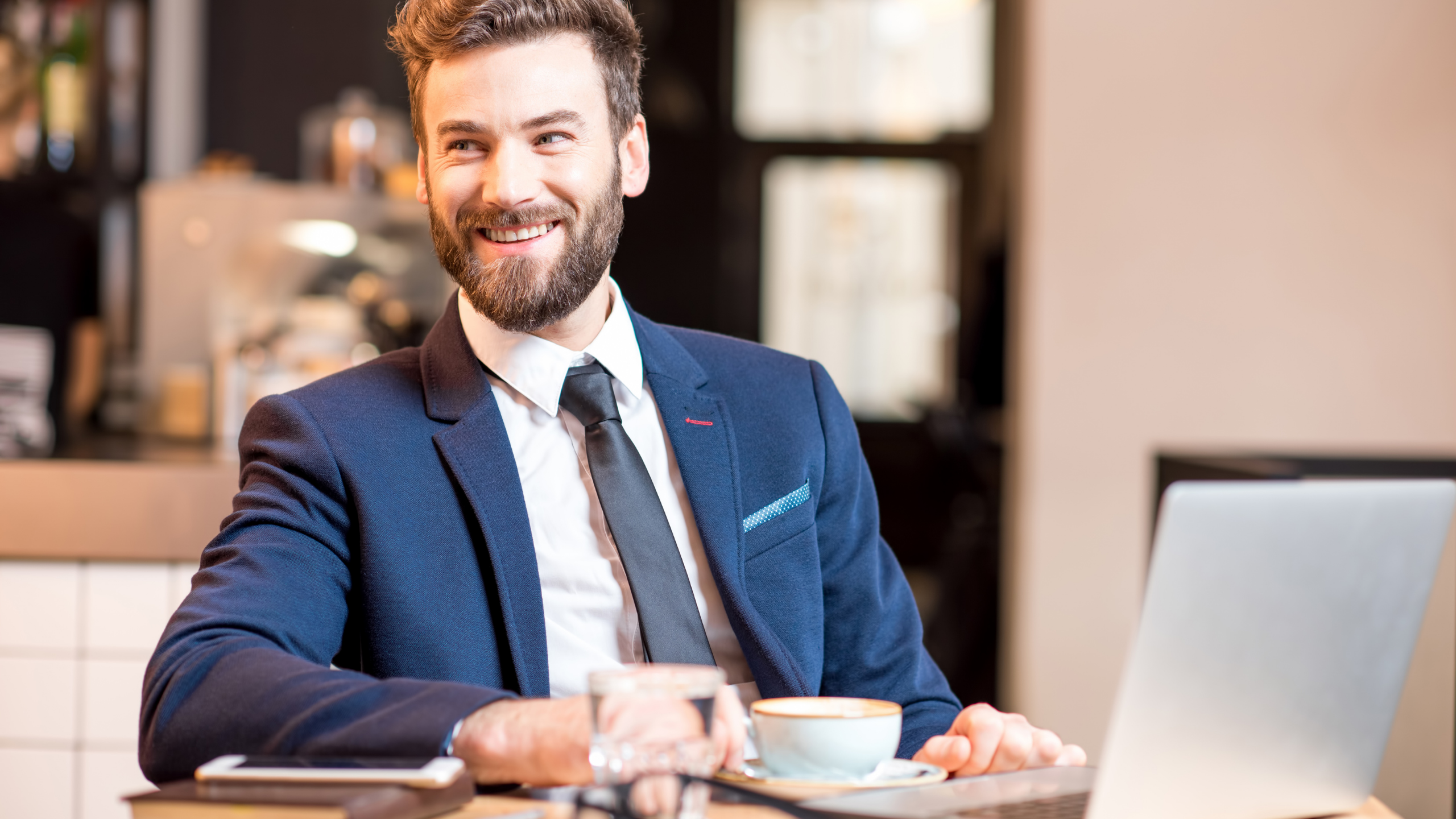 en mann sitter med laptop og drikker kaffe